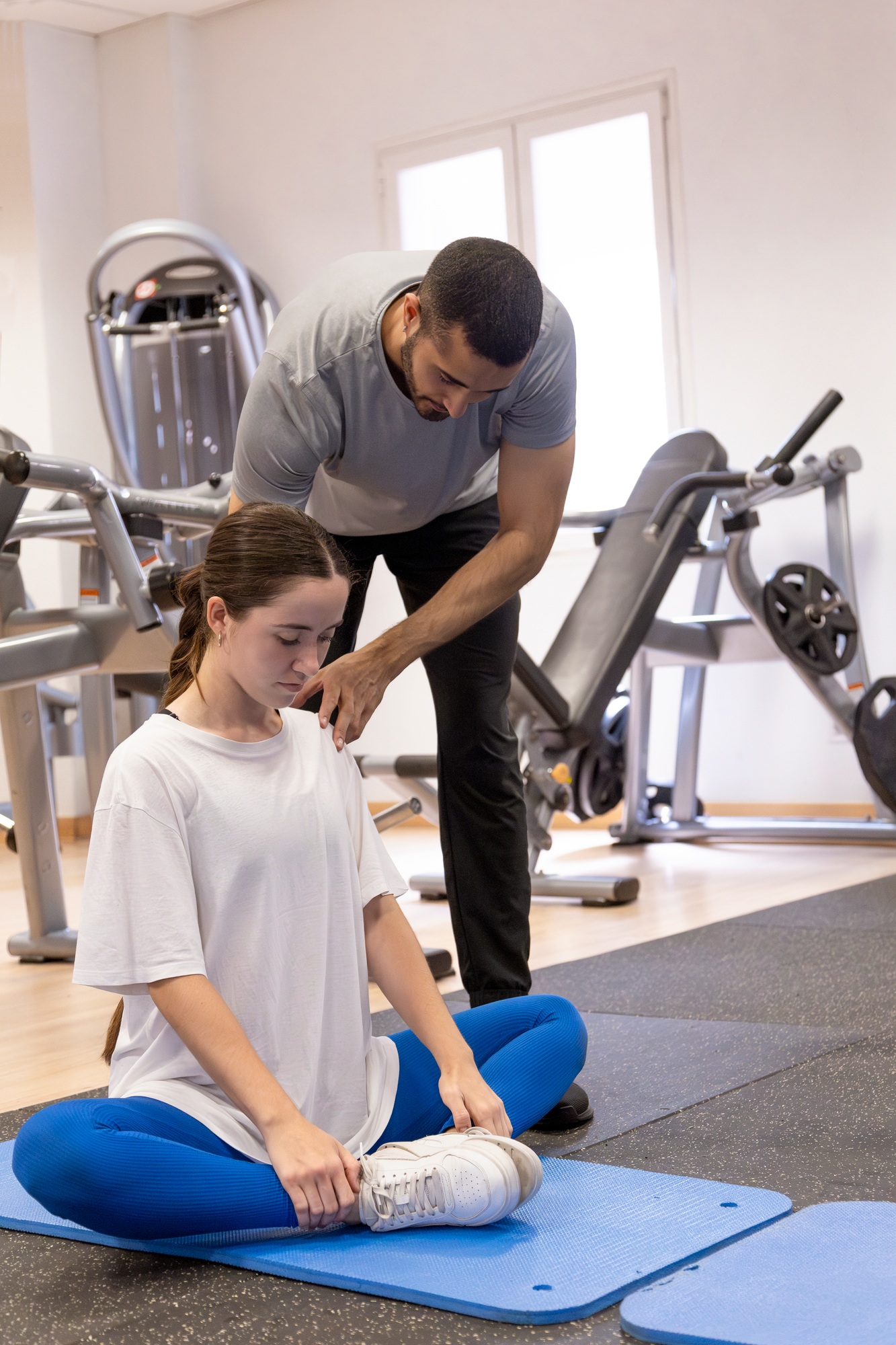 Trainer corrects woman's back posture during gym stretch