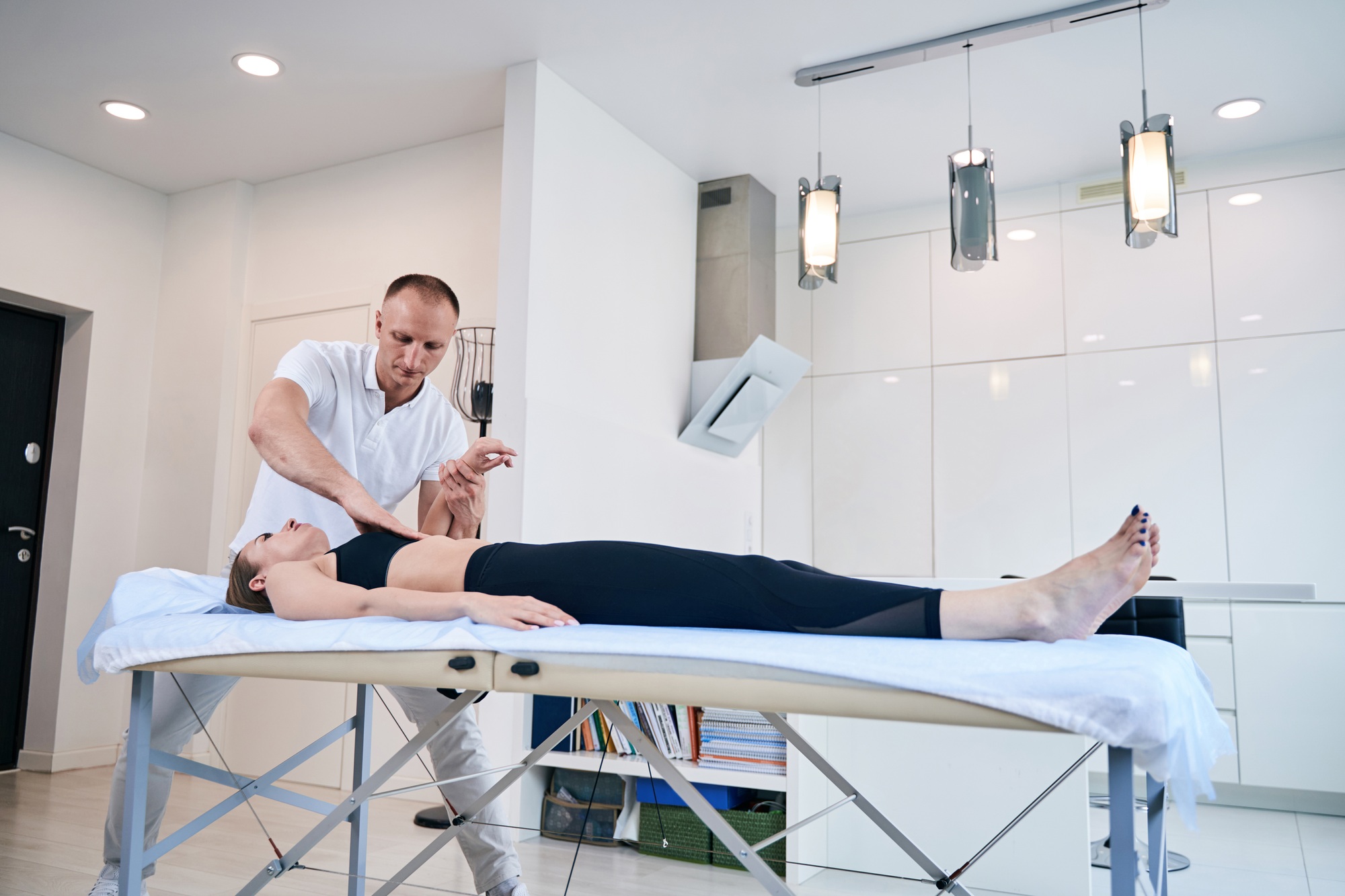 Young woman lying on medical couch while getting manual therapy session in medical office